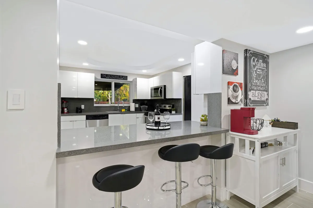 This image features a modern kitchen island with bar stools, decorative wall art, and a clearly visible coffee station. The space is open and inviting, designed for cooking, casual dining, and socializing. The coffee station integrates seamlessly into the kitchen, making it a focal point for coffee lovers.