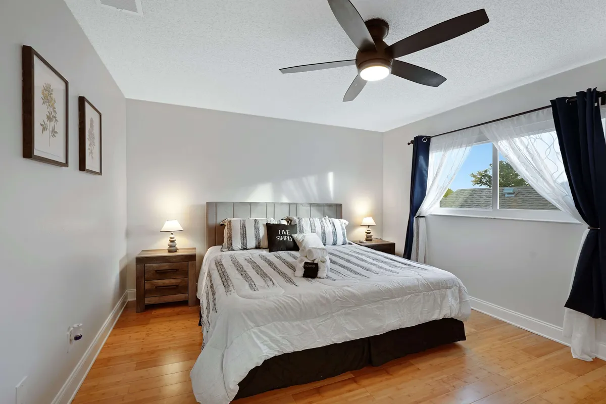 A tranquil bedroom featuring a spacious bed with cozy bedding, flanked by nightstands and illuminated by natural light filtering through the window. Decorative art adds a soothing touch, and the overall atmosphere is calm and inviting.