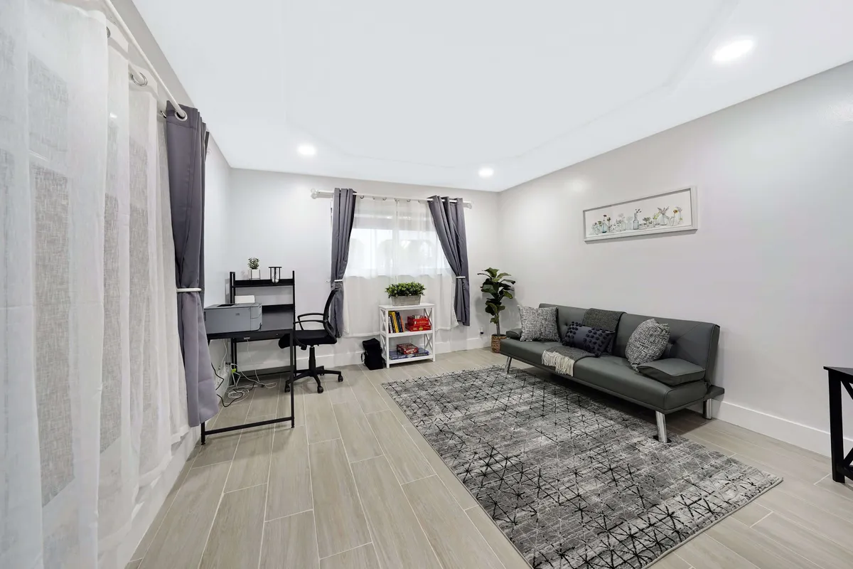 A serene living area featuring a sofa, a desk for flexible use, soft curtains, a lush potted plant, and a cozy rug. The atmosphere feels tranquil and inviting, ideal for group games, family chats, or simply unwinding.